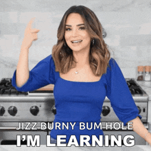 a woman in a blue top is standing in front of a stove and says jizz burny bum hole i 'm learning