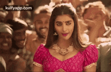 a woman in a pink blouse and gold necklace is standing in front of a crowd .