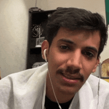 a man with a mustache wearing ear buds and a white lab coat