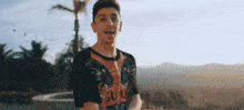 a young man wearing a gucci t-shirt is standing in front of a palm tree .