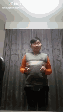 a young boy is standing in front of a curtain with a tik tok watermark on the bottom