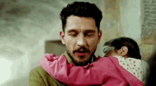 a man with a beard is holding a baby in a pink jacket .