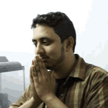 a man in a plaid shirt prays with his hands folded