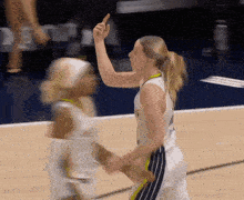 two female basketball players are playing a game and one of them is pointing up