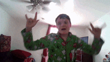 a young boy in a green pajama shirt is making a devil horns gesture