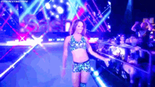 a female wrestler is walking on a stage with a crowd watching .