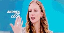 a woman is waving her hand in front of a blue background with andrea joy cook written on it .