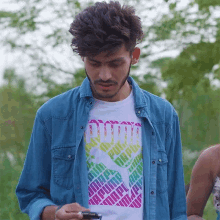 a man wearing a blue shirt and a white puma t-shirt looks at his phone