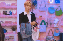 a man in a suit is standing in front of a pink wall holding a jacket and a bag .