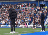 two men standing on a soccer field in front of a premier league banner