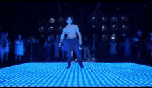 a shirtless man is dancing in a dark room with blue light behind him .