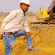 a man wearing a white hard hat is kneeling down in front of a yellow excavator