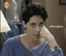 a woman in a blue shirt is sitting in front of a lamp .
