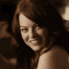a woman with red hair is smiling and looking over her shoulder at a man .