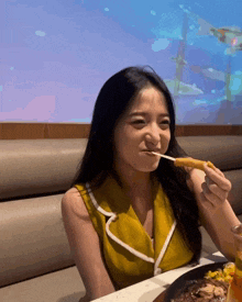 a woman in a yellow top is eating a french fry