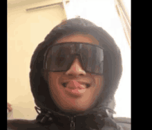 a man wearing sunglasses and a hoodie is sticking his tongue out .