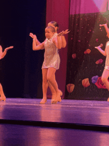 a group of young girls are dancing on a stage in front of a pink curtain with flowers on it