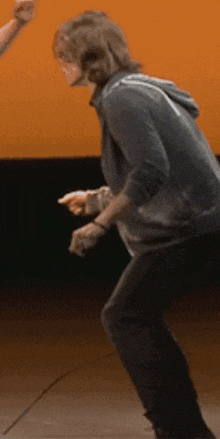 a man in a hoodie is dancing in front of a yellow wall