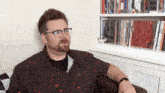 a man wearing glasses is sitting in front of a bookshelf filled with books