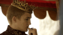 a man wearing a crown and a ring is smoking a cigarette .