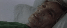 an elderly woman is laying in a hospital bed with a green blanket on .