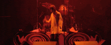 a man is singing into a microphone on a stage with a drummer in the background .