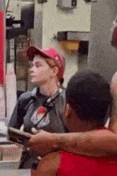 a woman in a red hat is standing in front of a man in a red shirt in a restaurant .