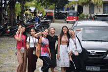 a group of girls posing for a picture in front of a silver toyota