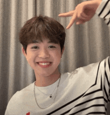 a young man wearing a striped shirt and a necklace is making a heart shape with his fingers
