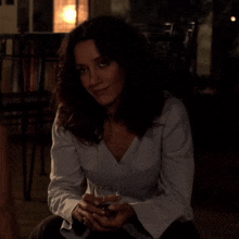 a woman in a white shirt is holding a glass
