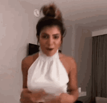 a woman in a white halter top is standing in a room with her hair in a bun .