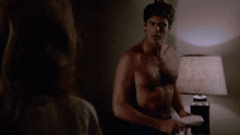 a shirtless man stands in front of a lamp in a dark room