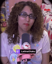 a woman with curly hair wearing glasses and a hello kitty shirt is holding a pink microphone