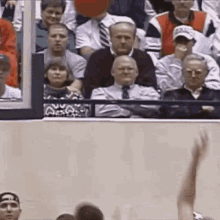 a group of people are watching a basketball game and one of them is raising his hand in the air .