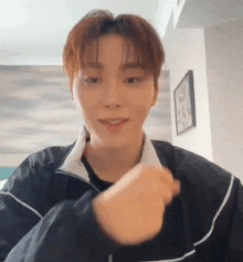 a young man in a black jacket is making a heart shape with his hand .