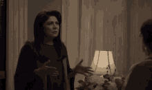 a woman is talking to another woman in a living room with a lamp .