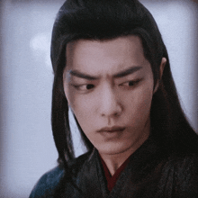 a close up of a young man with long black hair making a serious face .