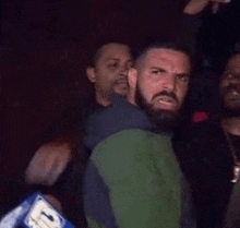 a man with a beard and a green jacket is standing in a crowd .