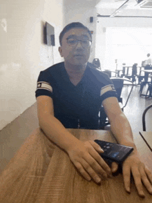 a man sits at a table with his hands folded and a cell phone on his lap