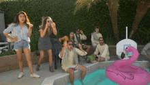 a group of people are gathered around a pool with a pink flamingo float