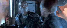 a man in a leather jacket is standing next to another man with a robotic face .