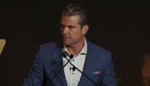 a man in a blue suit and white shirt is speaking into two microphones
