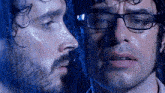 a man with glasses and a beard is looking at his reflection in a window