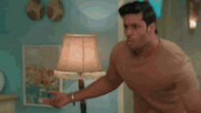 a man in a brown shirt is standing next to a lamp in a room .