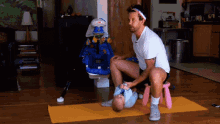 a man sitting on a pink stool with a baby on a yoga mat