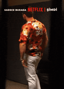 a man in an orange shirt and white pants stands in front of a sign that says netflix