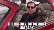 a man in a suit and tie is driving a red car with the words `` it 's britney bitch and i am back ''