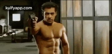 a shirtless man is holding a gun in his hand in front of a window .