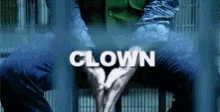 a man in a green jacket is sitting in a jail cell with the word clown written above him
