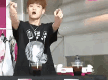 a man in a black shirt is standing in front of a table with two cups of coffee on it .